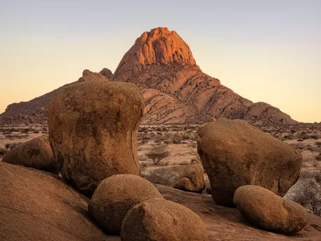 Large rocks in the foreground and a tall rocky mountain in the background in the Red Dunes of Sossusvei in Namibia.