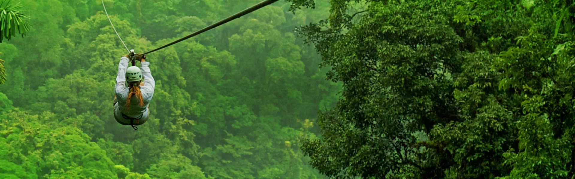Helmeted woman ziplines downhill in the middle of nature