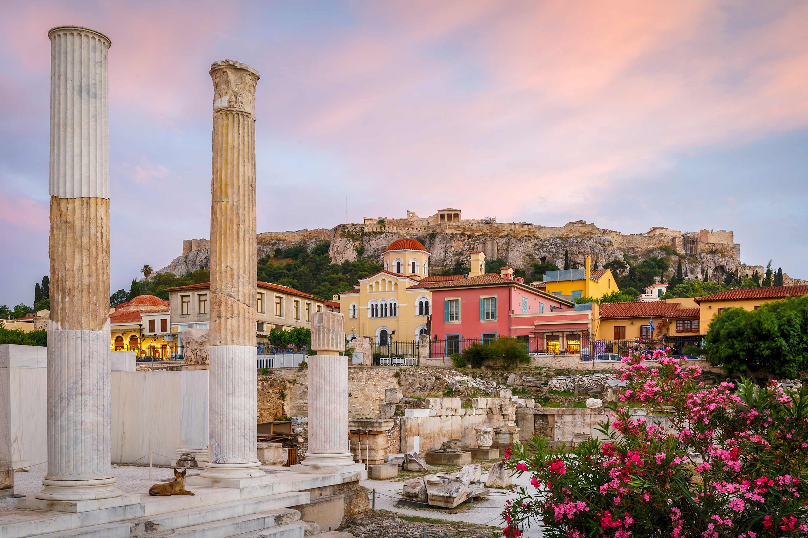 Historic ruins framed by vibrant houses under a pink evening sky in Athens, Greece