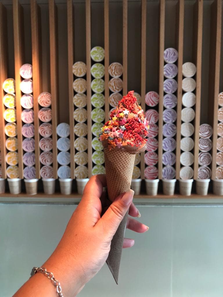 Hand holding up a multi-coloured Gelato in a cone