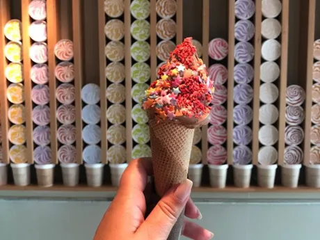 Hand holding up a multi-coloured Gelato in a cone