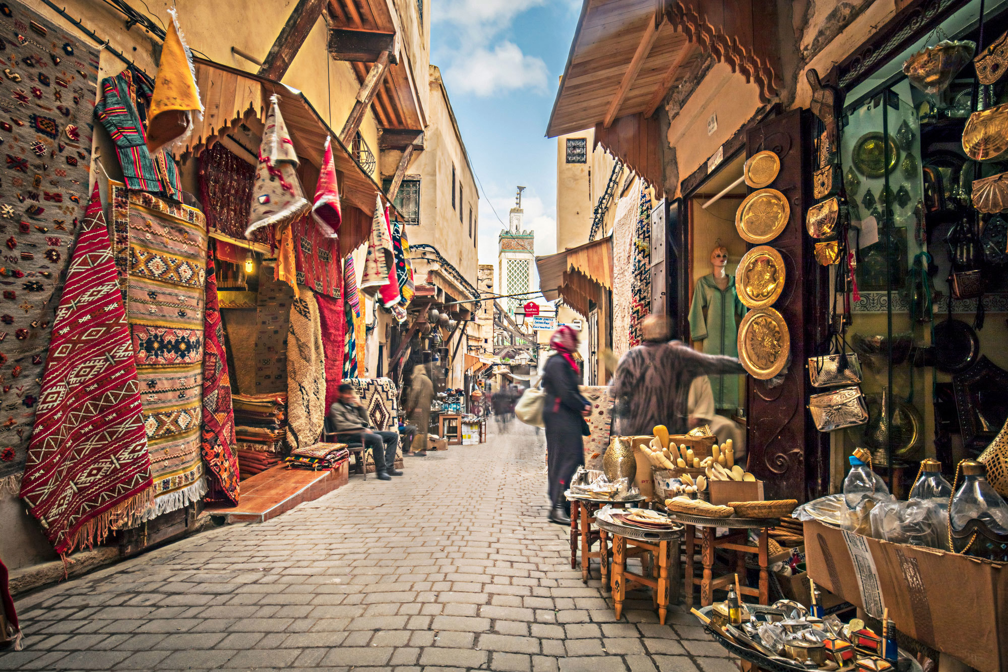 Narrow souk street  lined with colourful rugs and brassware shop in Fez, Morocco