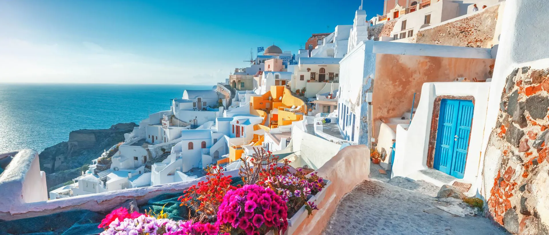 Santorini, Greece view of traditional cycladic Santorini houses on small street with flowers in foreground - Oia village