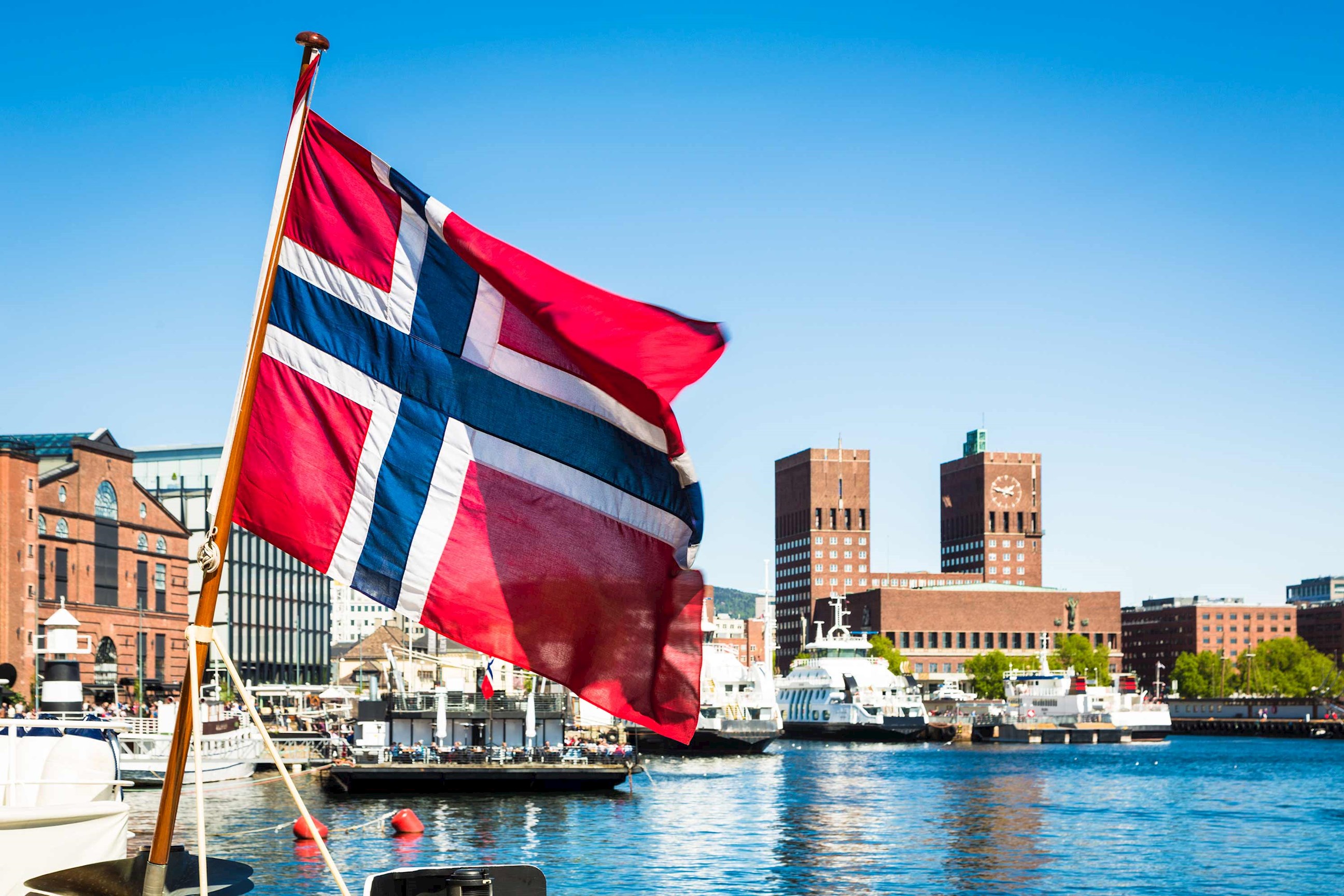 Norwegian flag waving near waterfront with boats and city buildings in Oslo, Norway