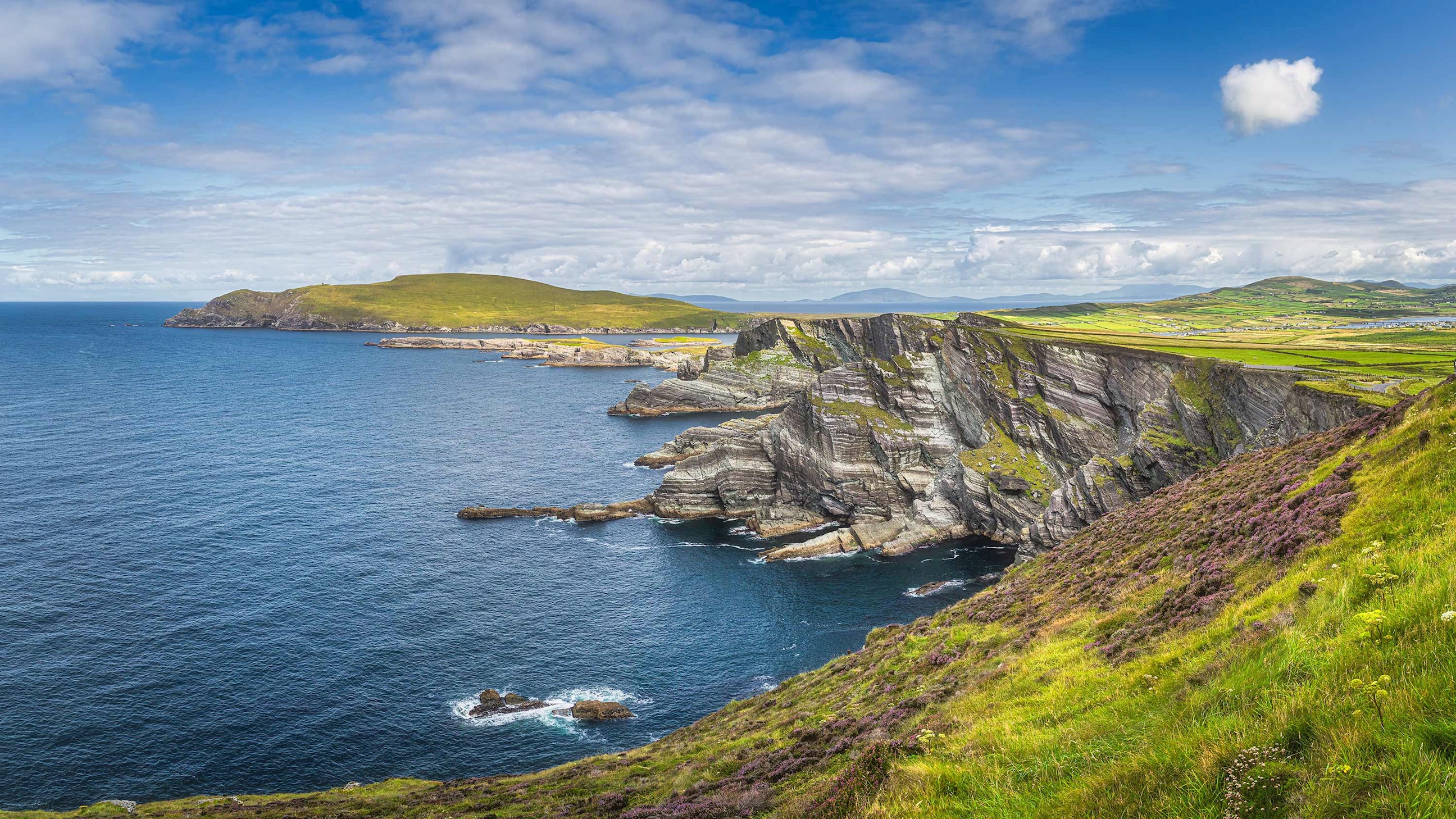Coastal cliffs overlooking deep blue ocean and green hills in The Ring of Kerry, Ireland