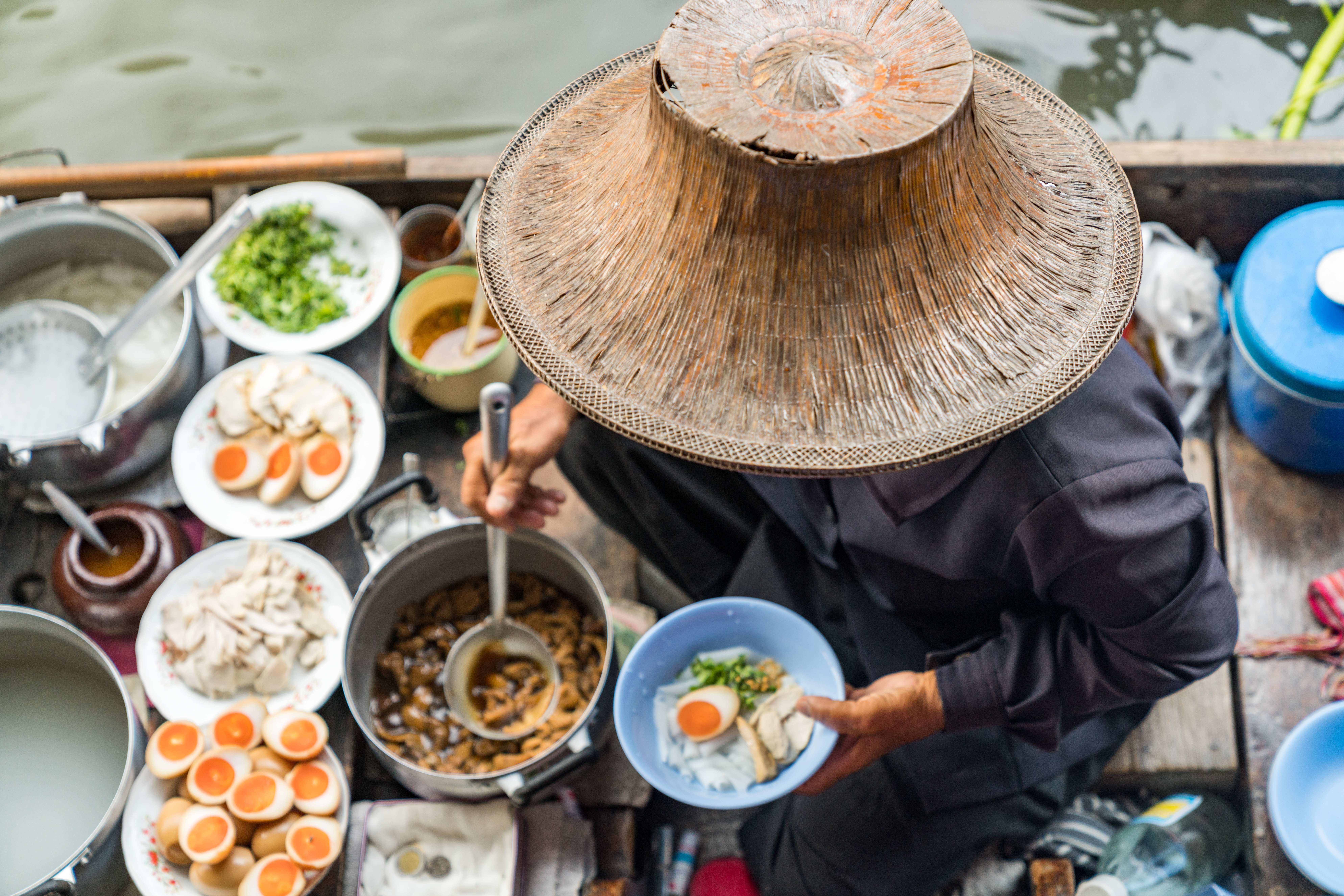 Birds-eye view of man in hat serving Asian cuisine on boat