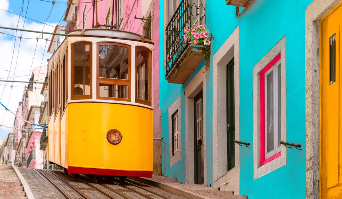 A yellow trolley car going down a street near colorful buildings