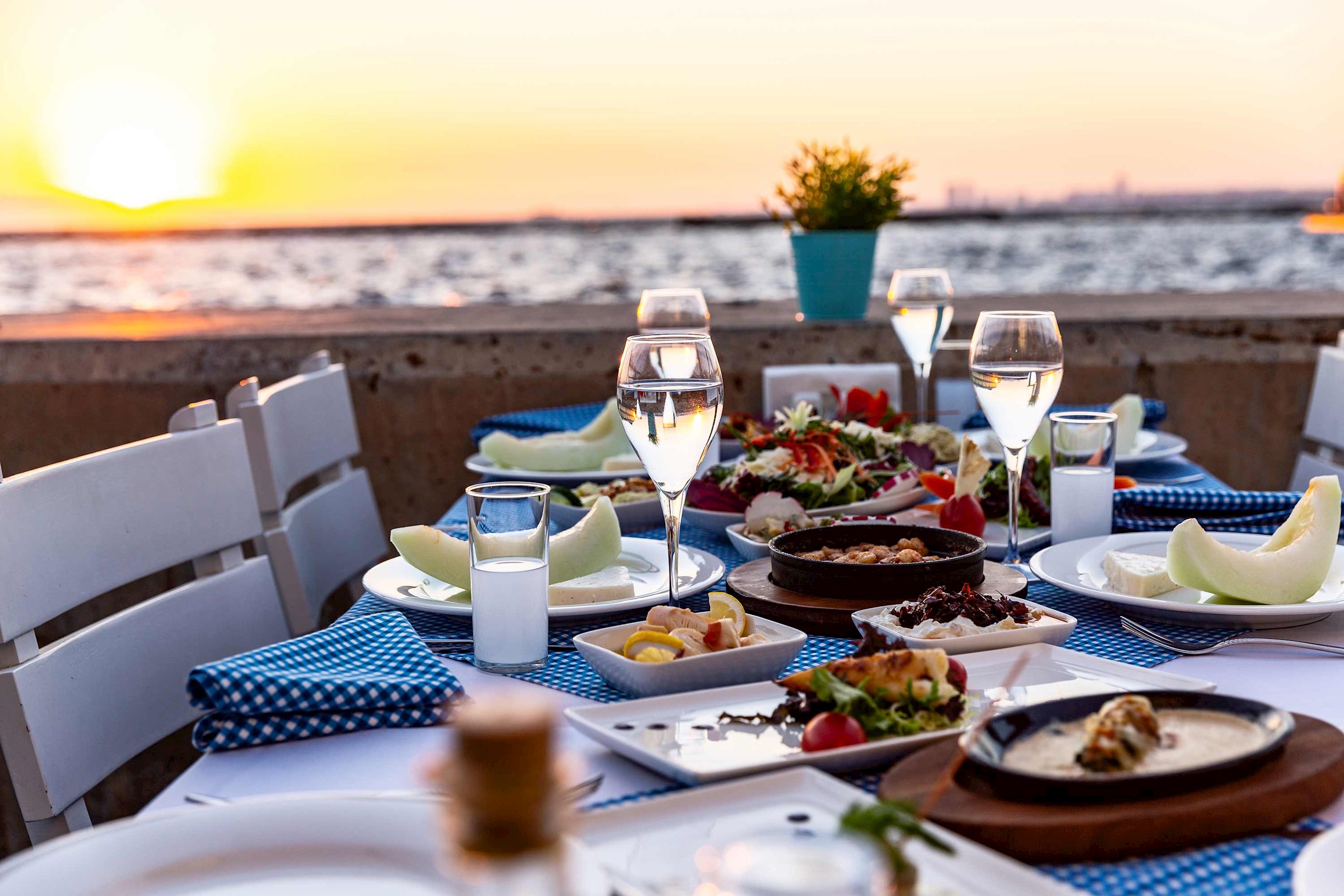 Outdoor seaside dinner with seafood dishes and drinks at sunset, Izmir, Turkey