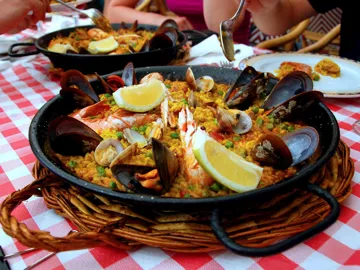 Seafood paella served in a black pan with mussels, clams, shrimp and lemon wedges on a checkered tablecloth