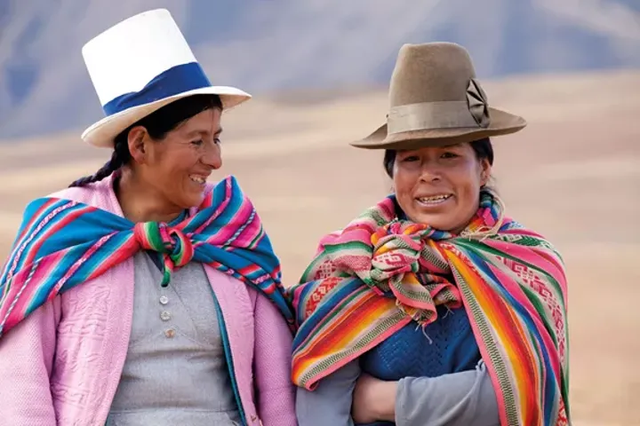 Two Women In Traditional Costume Walking In The Mountains Near Moray Peru