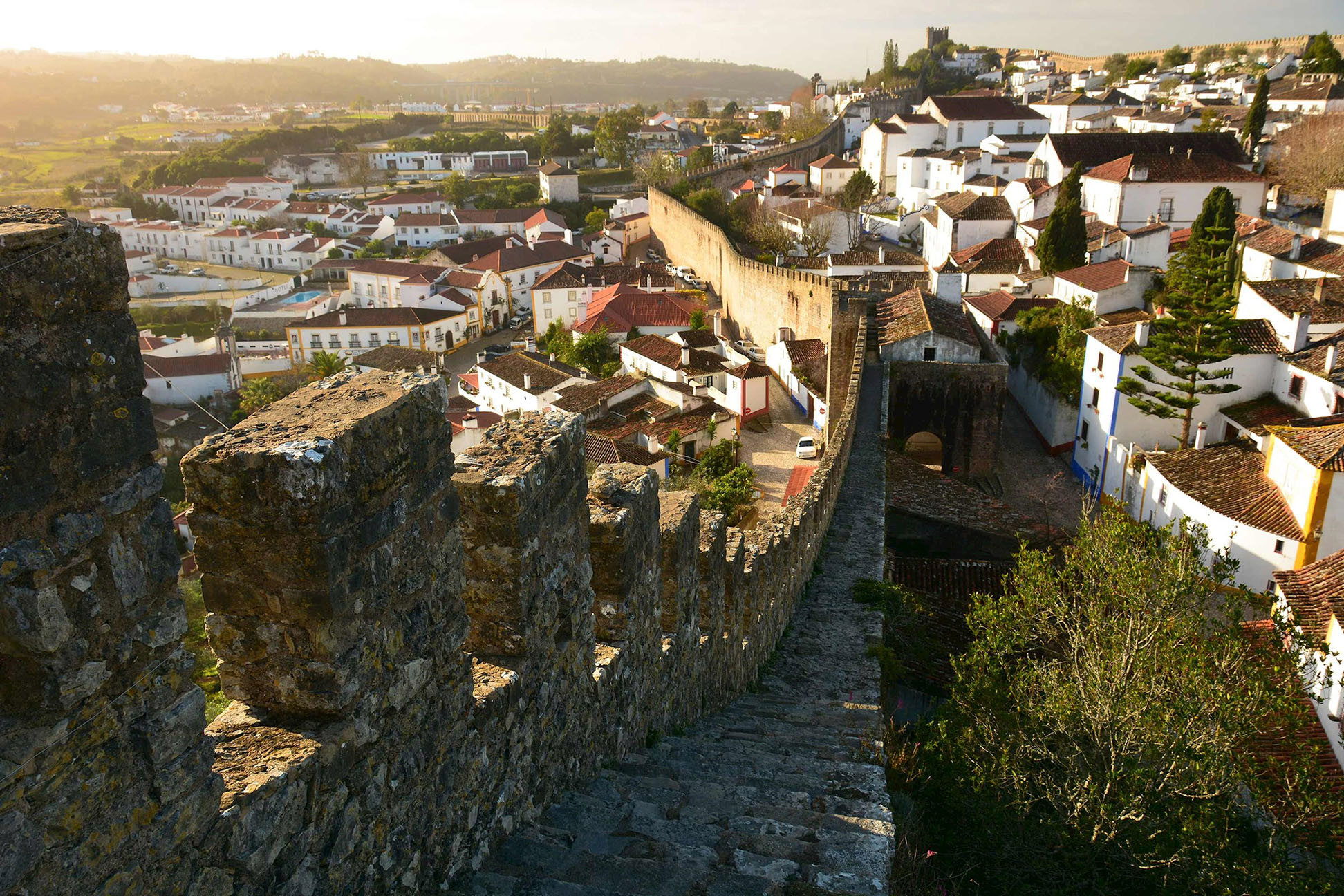 Stone wall walkway overlooking rooftops at sunset in Obidos, Portugal 