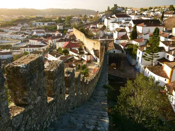 Stone wall walkway overlooking rooftops at sunset in Obidos, Portugal