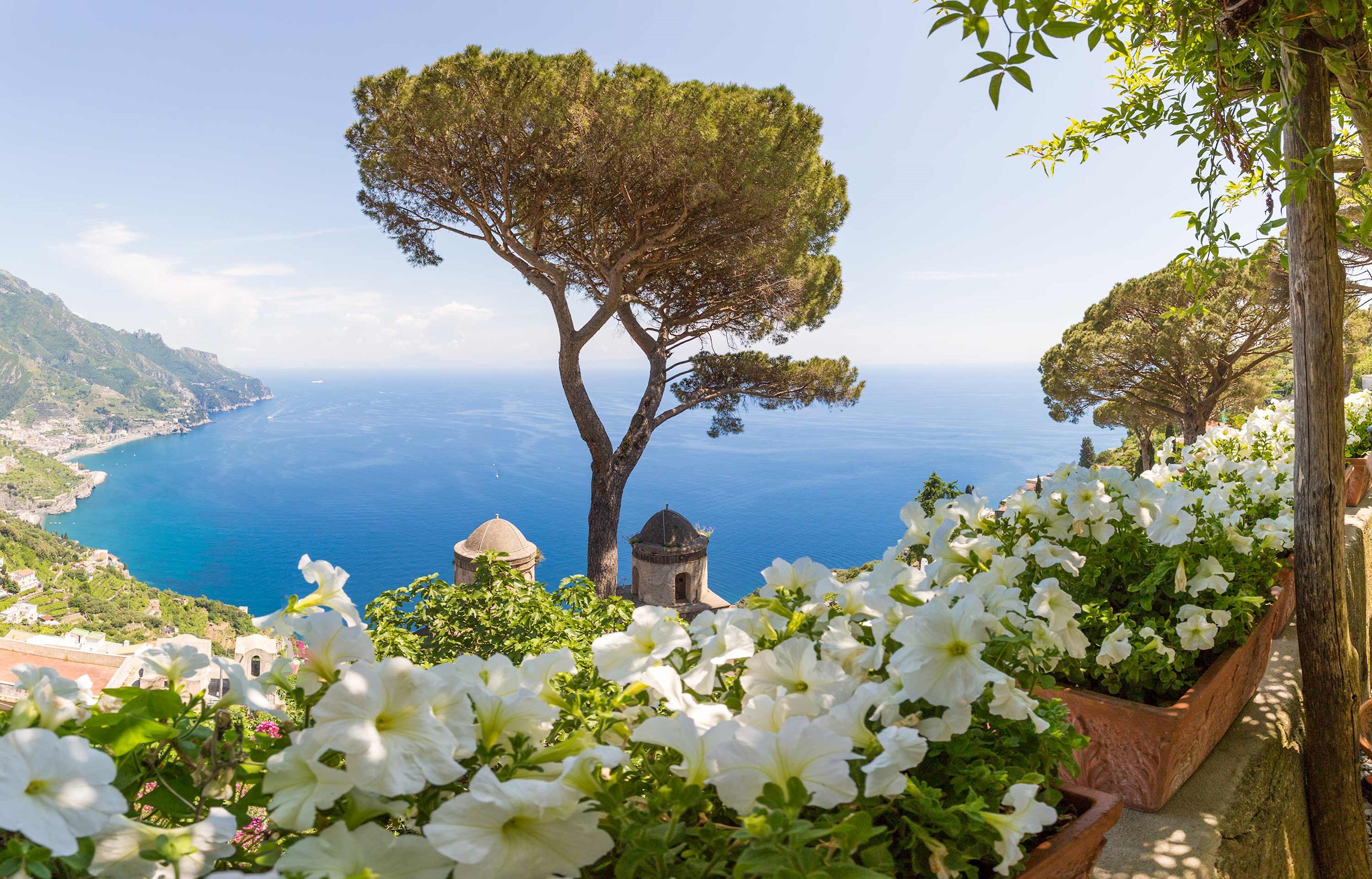 Close view of a flower-lined terrace overlooking the blue sea and distant hills in Sorrento, Italy
