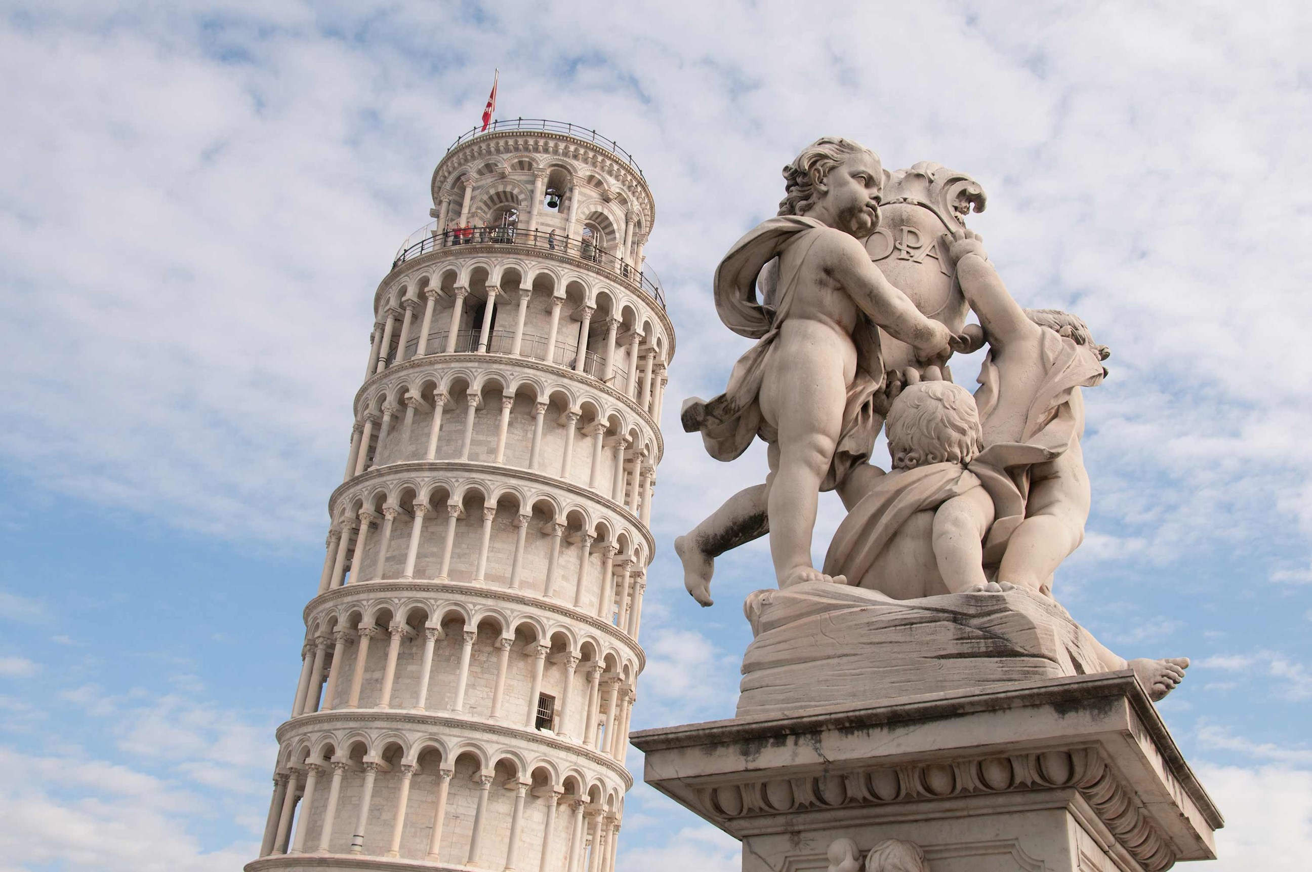 Close view of the Leaning Tower of Pisa and a statue in Pisa, Italy