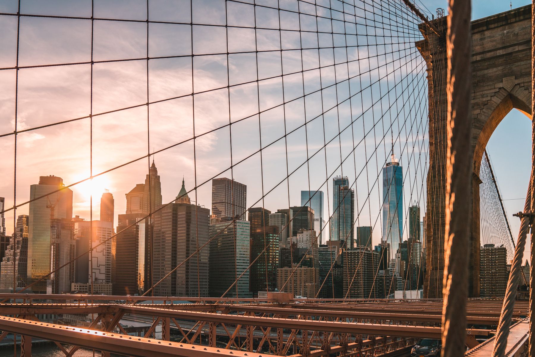 The skyline of New York City with the Brooklyn Bridge in the foreground and the setting sun behind.