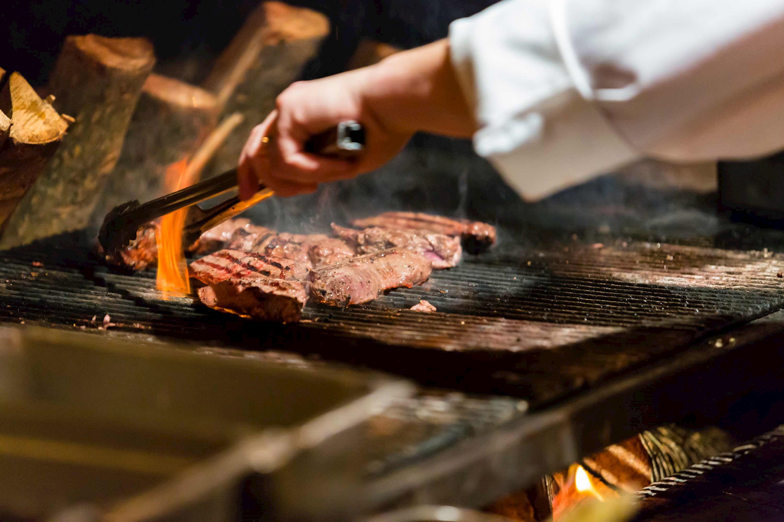Close-up of chef’s hand grilling steaks over open flame