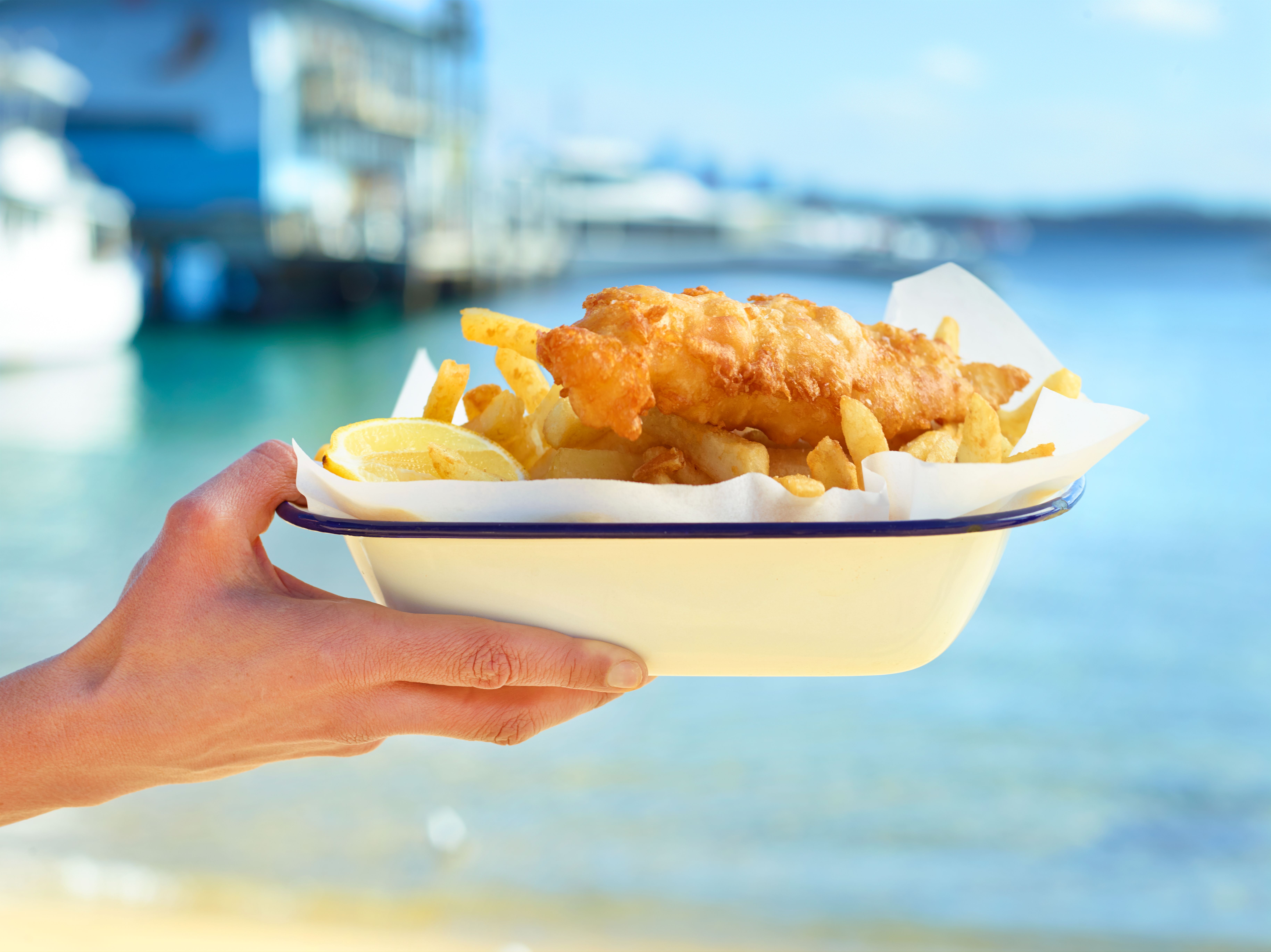 Traditional fish and chips being held up in front of the sea
