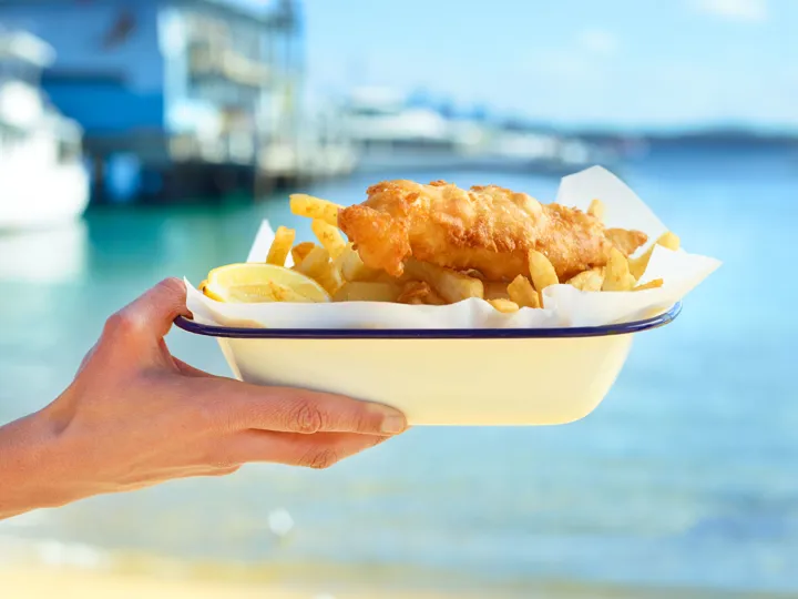 Traditional fish and chips being held up in front of the sea