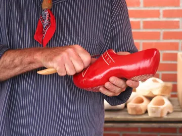 Person carving details into a red wooden clog by hand