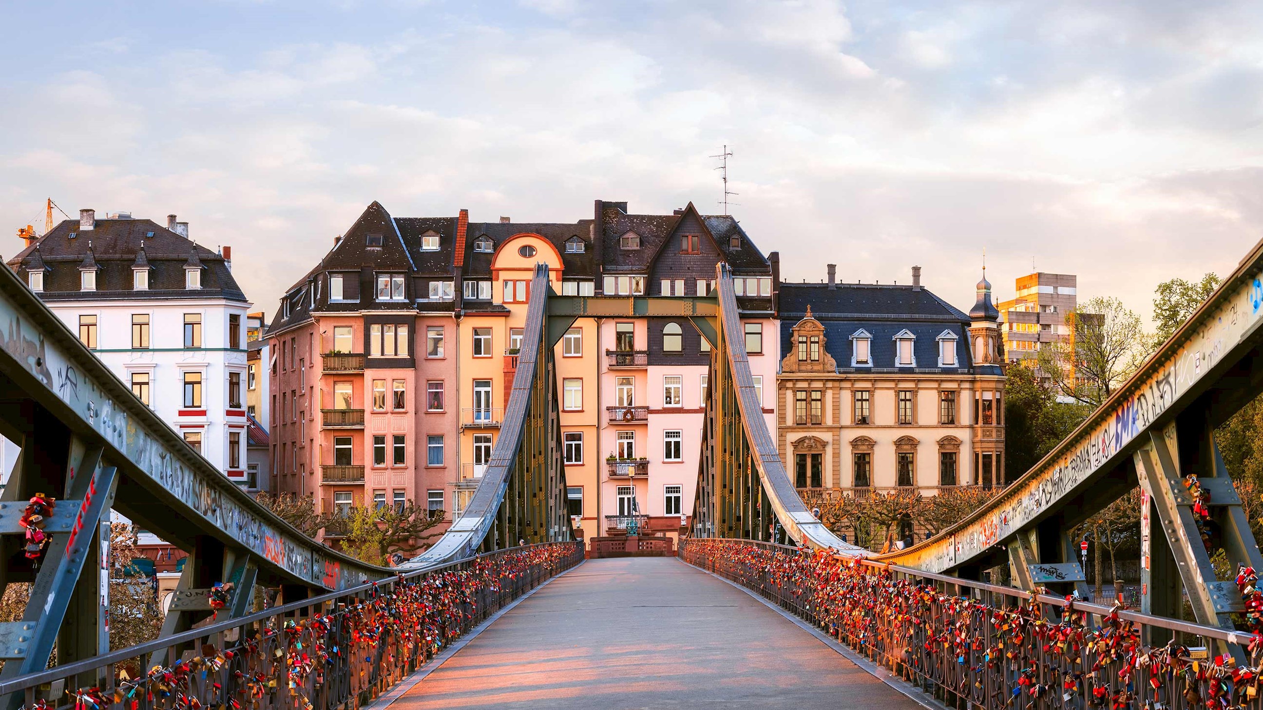 Pedestrian bridge lined with love locks leading to historic buildings in Frankfurt, Germany