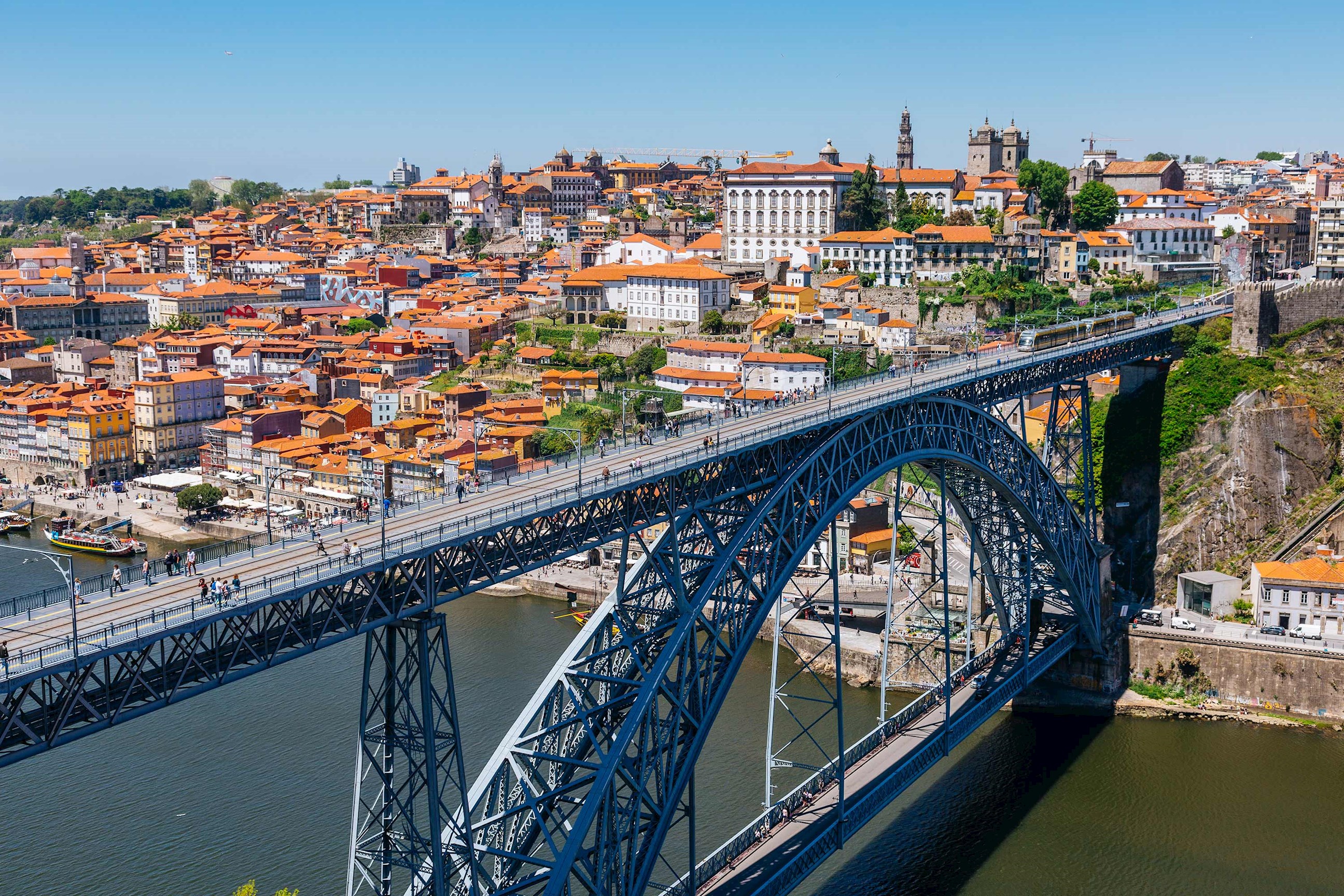 Steel arch bridge spanning river with city buildings in background in Porto, Portugal