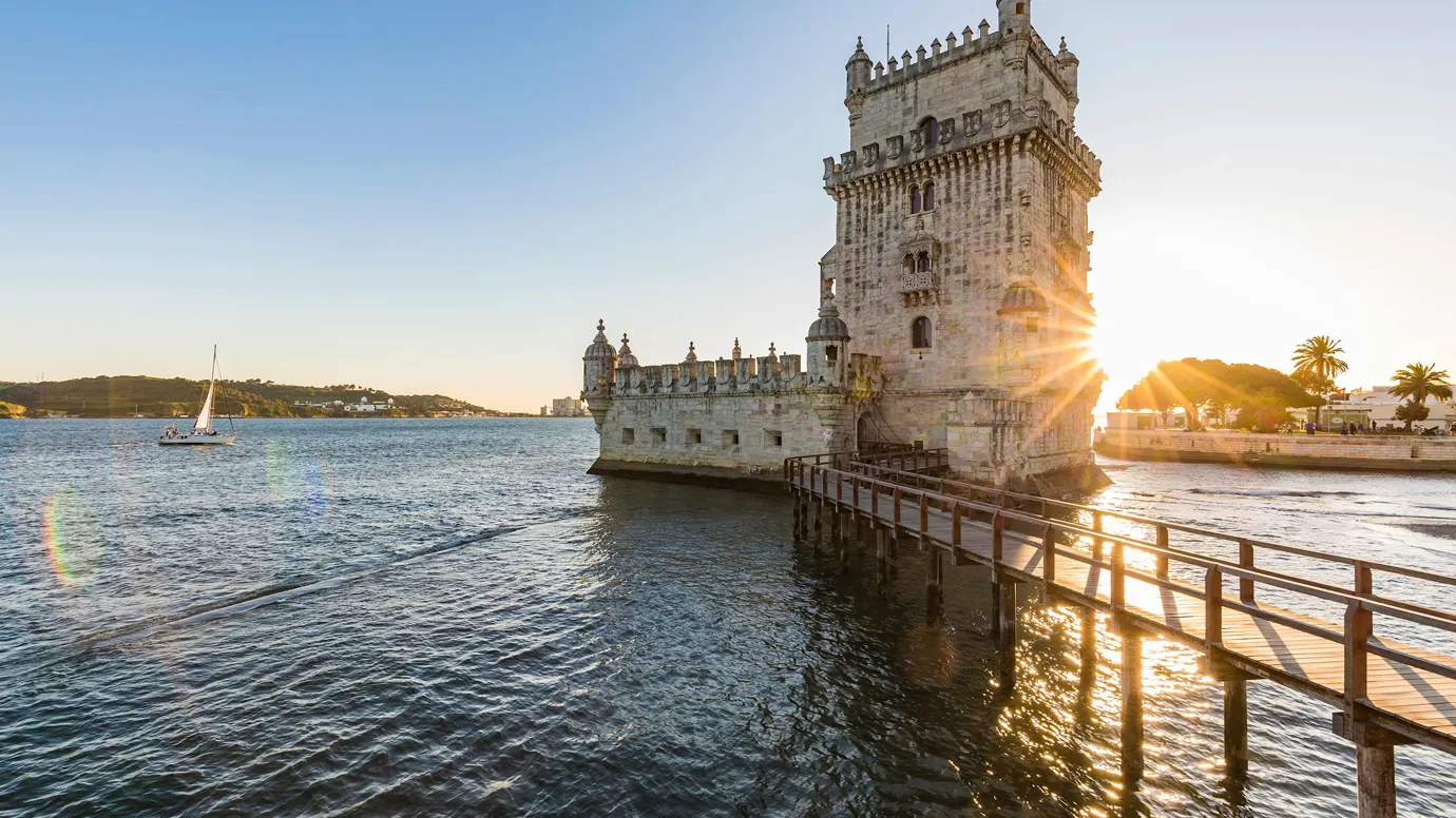Stone tower on waterfront with wooden walkway during sunset in Lisbon, Portugal