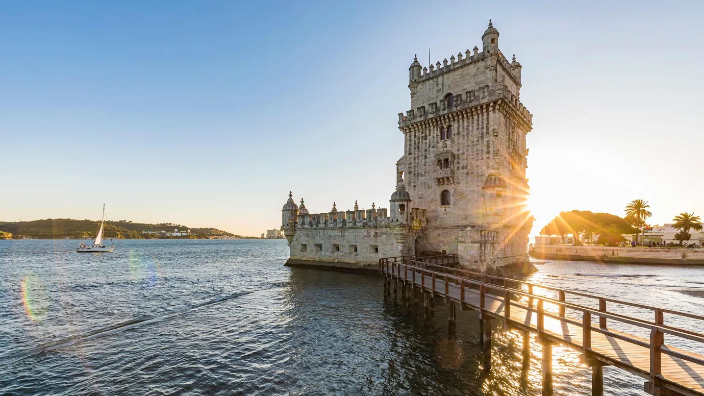 Stone tower on waterfront with wooden walkway during sunset in Lisbon, Portugal