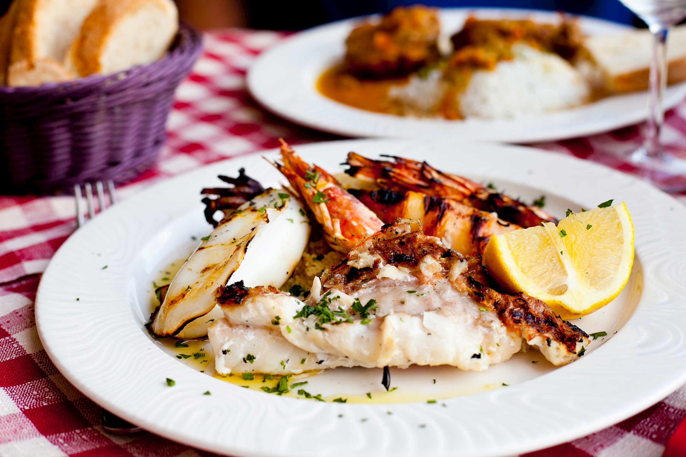 Plate of grilled seafood with lemon wedge on a checkered tablecloth