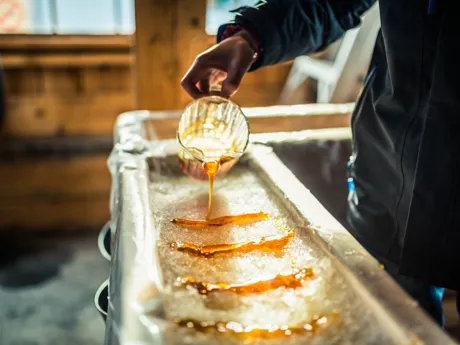 Person pouring Maple Syrup onto snow at Sugar Shack in Canada