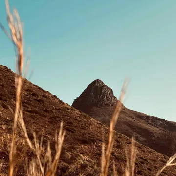 A stark, black rock mountain with brown grass in the foreground, Lionhead Mountain in South Africa