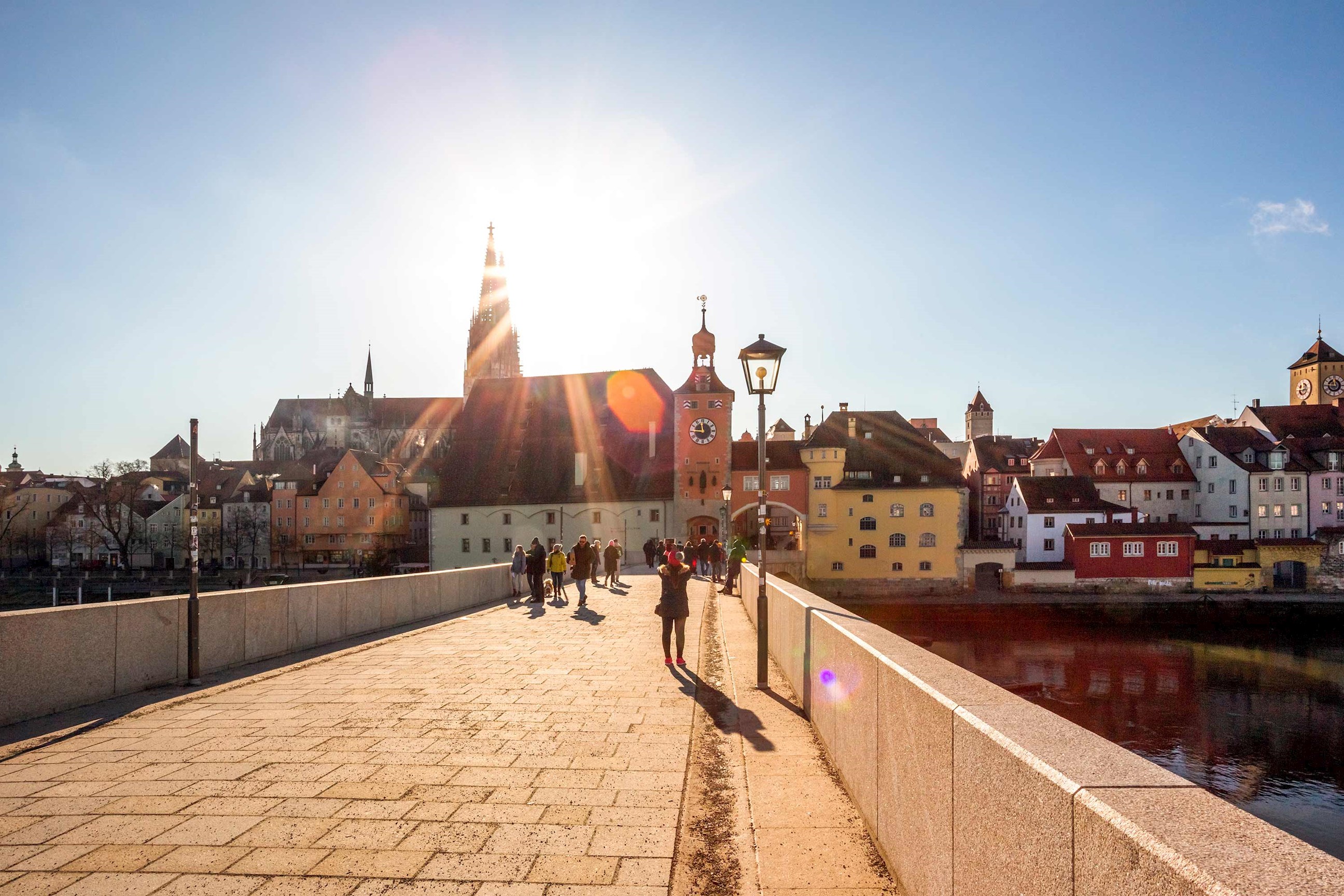 Stone bridge leading to buildings under bright sunlight in Regensburg, Germany