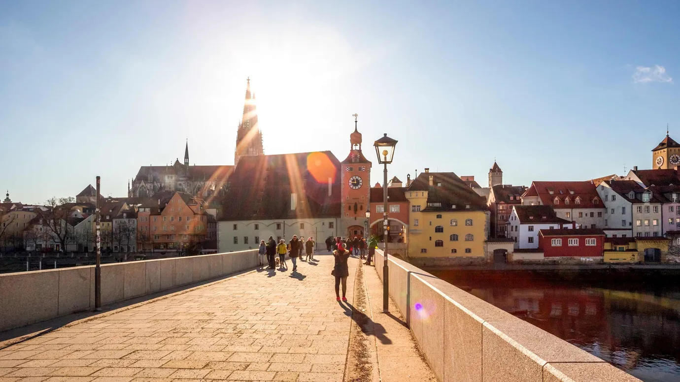 Stone bridge leading to buildings under bright sunlight in Regensburg, Germany