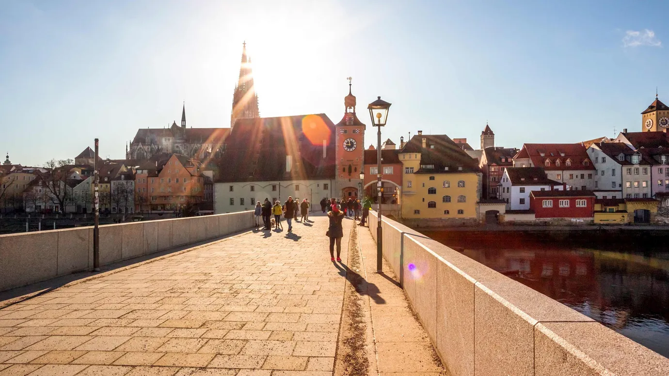 Stone bridge leading to buildings under bright sunlight in Regensburg, Germany