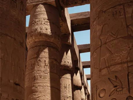 Tall columns covered in hieroglyphs with the sky visible above in a temple in Egypt