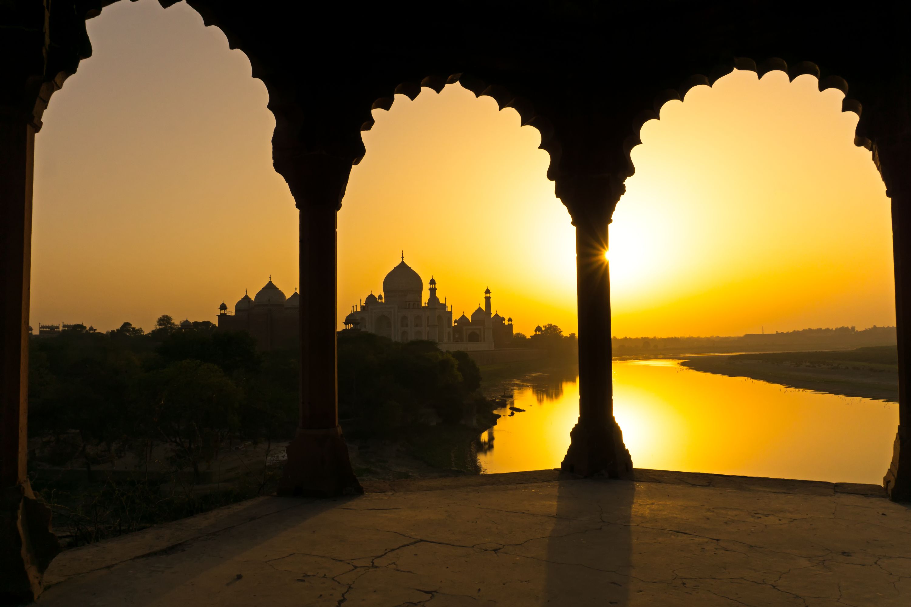 Looking through stone arches toward the Taj Mahal, at sunset. A must-do experience in India.