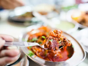Close-up of fork lifting curry from metal serving dish