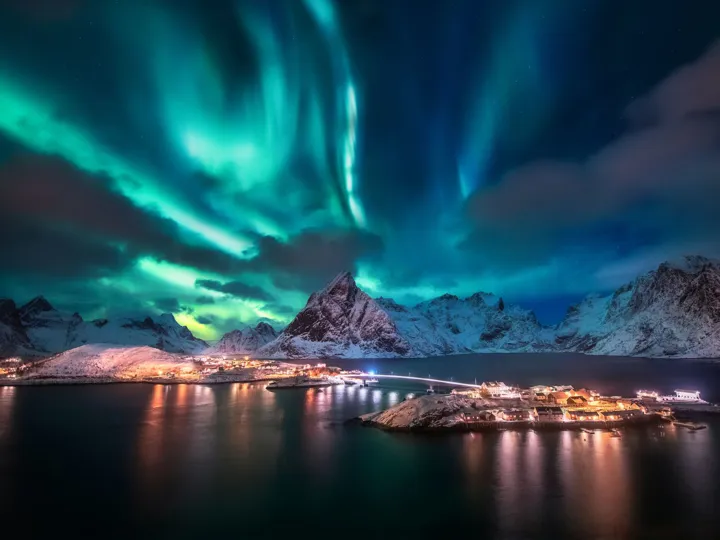Northern Lights over a mountain with a town on the water below