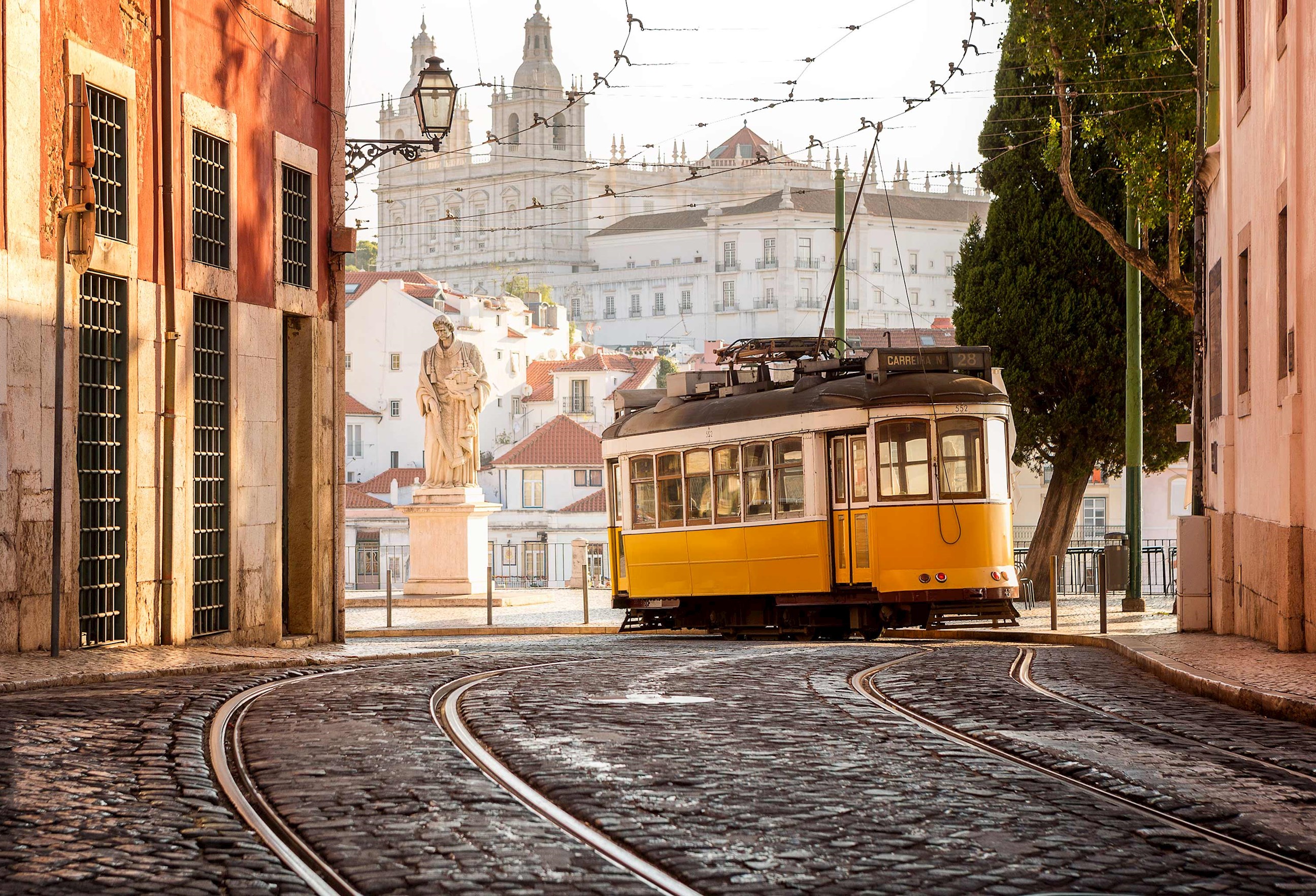 Yellow tram on cobblestone street with statue and historic buildings in Lisbon, Portgual