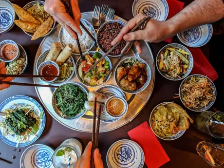 Traditional Thai Meal with many plates and people sharing using chopsticks, Thailand