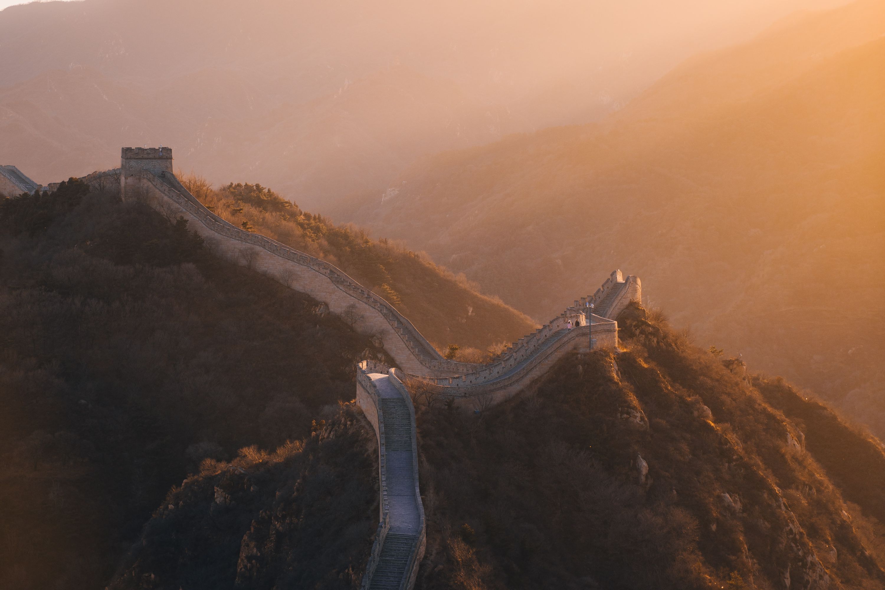 The Great Wall of China snakes over hilltops as the sun sets