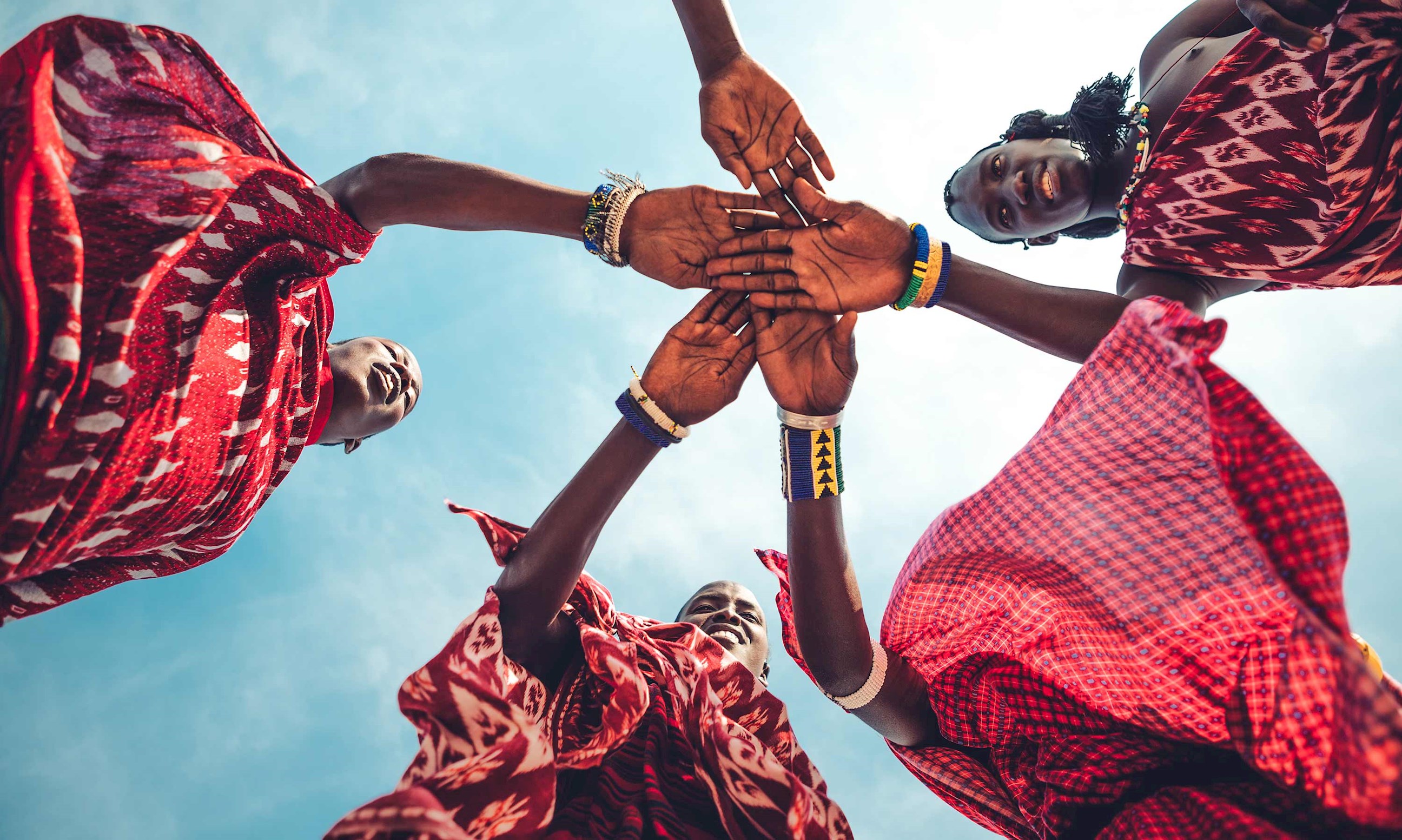 Maasai people joining hands in traditional attire under blue sky, Kenya