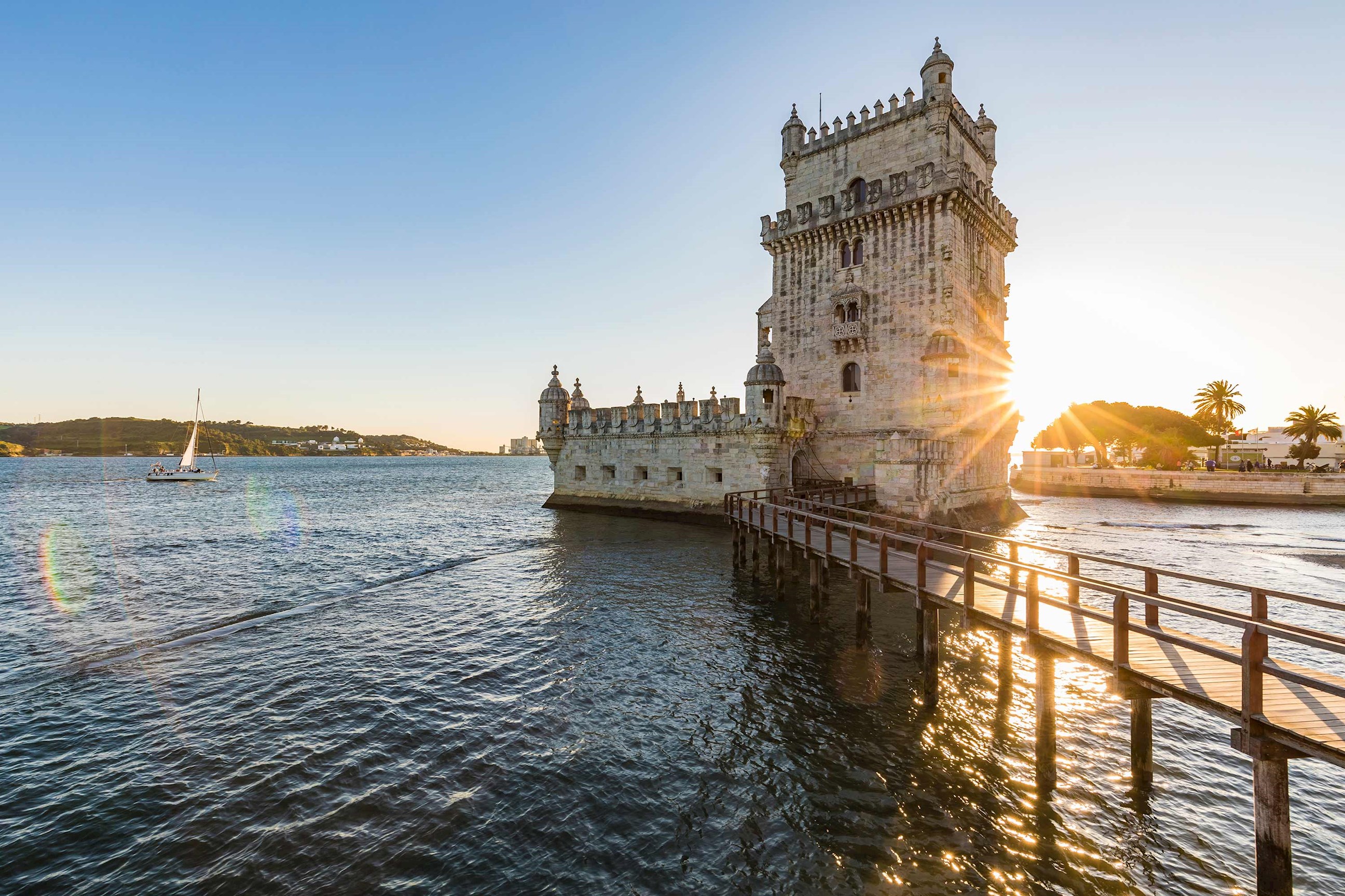 Stone tower on waterfront with wooden walkway during sunset in Lisbon, Portugal