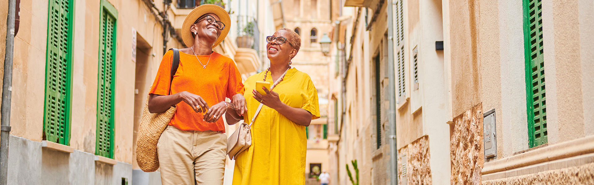 Two ladies, dressed in orange and yellow, smiling as they walk down a European cobbled street