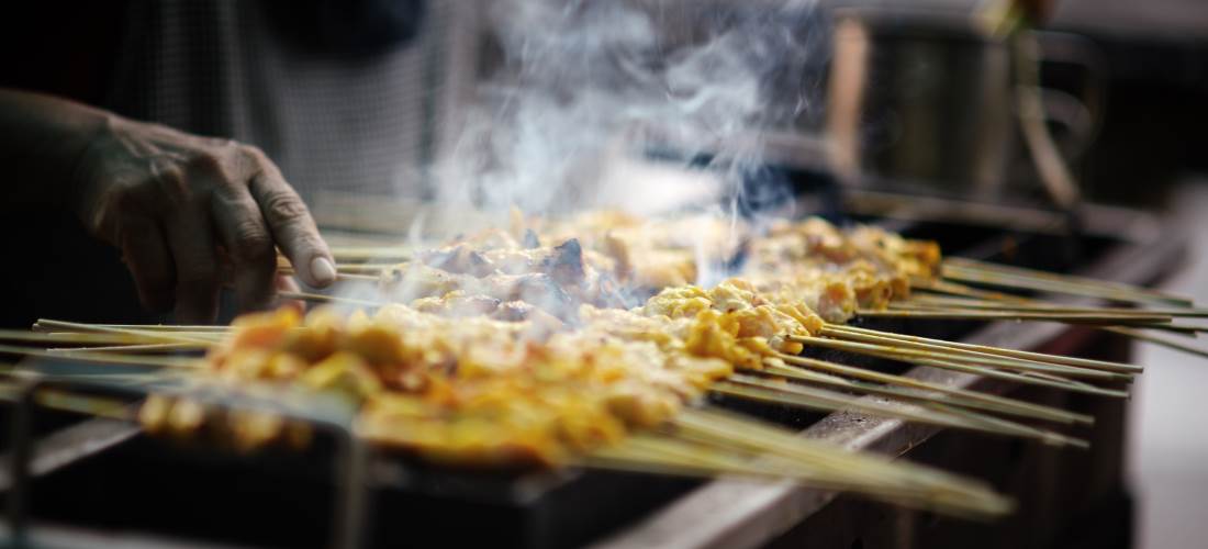 Skewers of meat satay cooking over a grill with steam rising from them. Typical cooking of Malaysia.