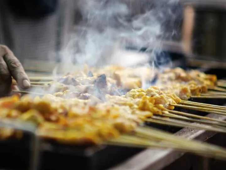 Skewers of meat satay cooking over a grill with steam rising from them. Typical cooking of Malaysia.
