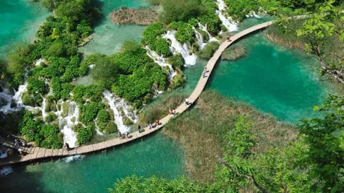 The aerial view of people walking across a bridge over a Plitvice lake in Croatia