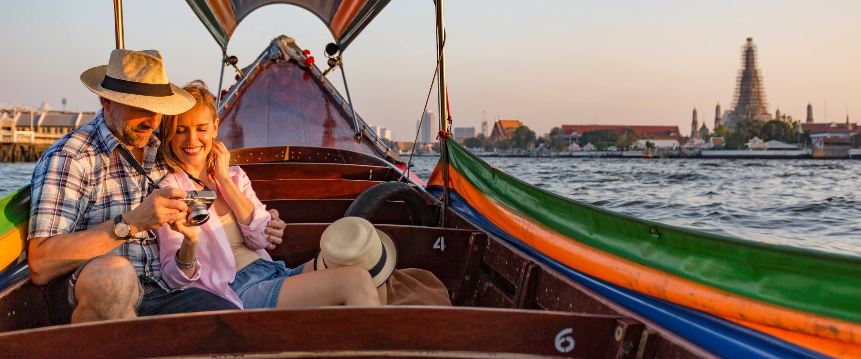 Couple on boat in Thailand, smiling and looking at a camera