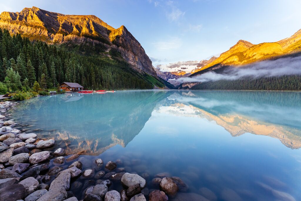 A view across Lake Louise in Canada. The lake is surrounded by mountains that look gold in the sunrise.