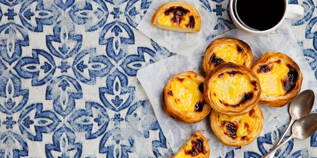 A blue and white table topped with pastel de nata next to a cup of coffee in Portugal