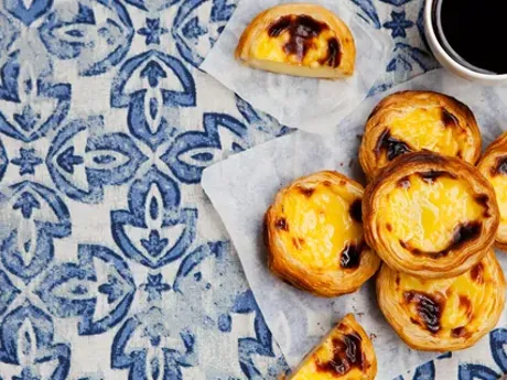 A blue and white table topped with pastel de nata next to a cup of coffee in Portugal